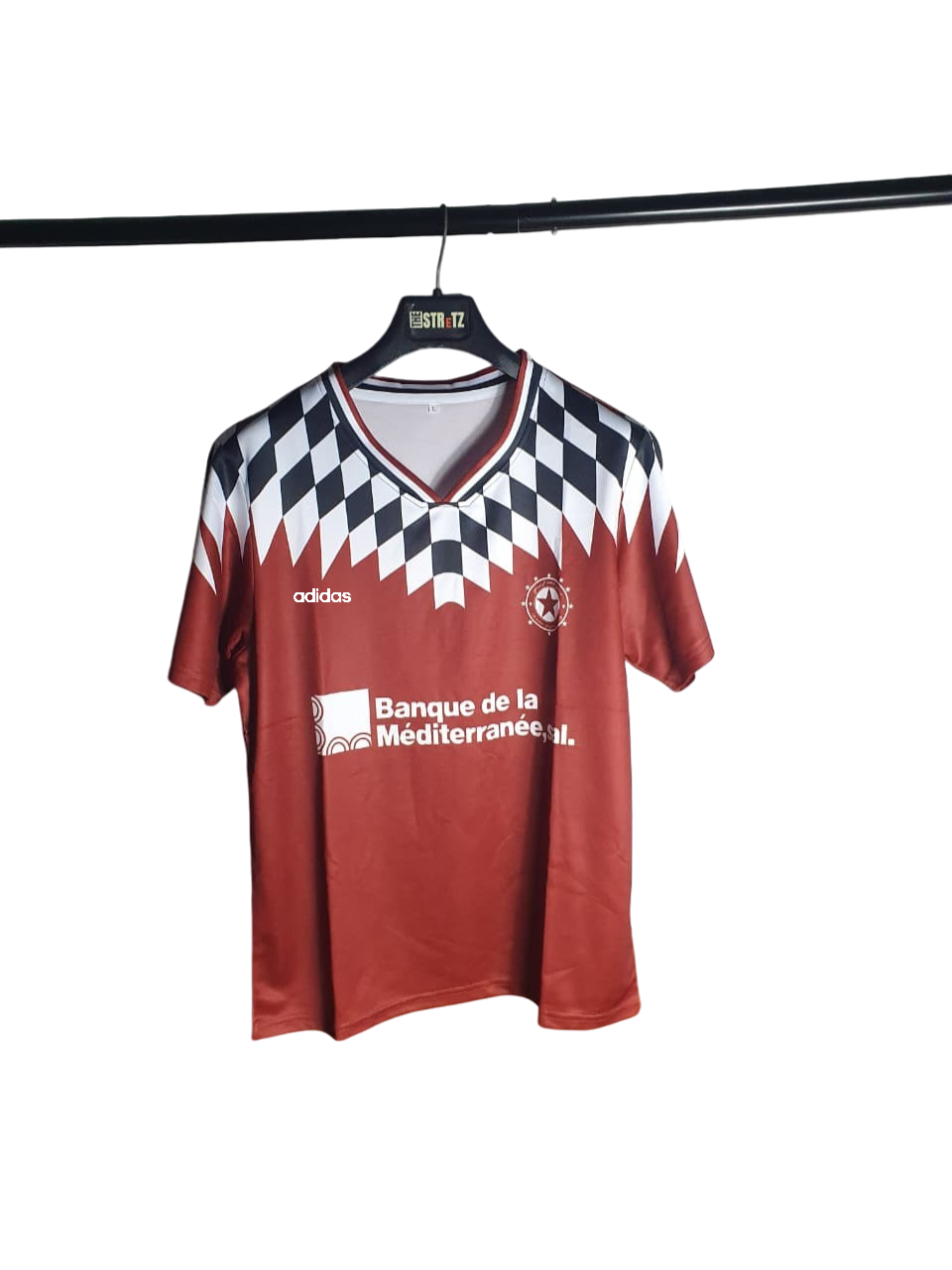 Red sports jersey with black and white checkered pattern on a hanger against a white background