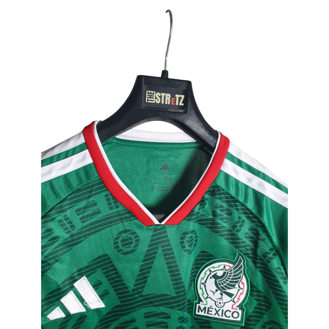Green soccer jersey with red and white accents, featuring a Mexico emblem, on a hanger with 'The Street' branding.
