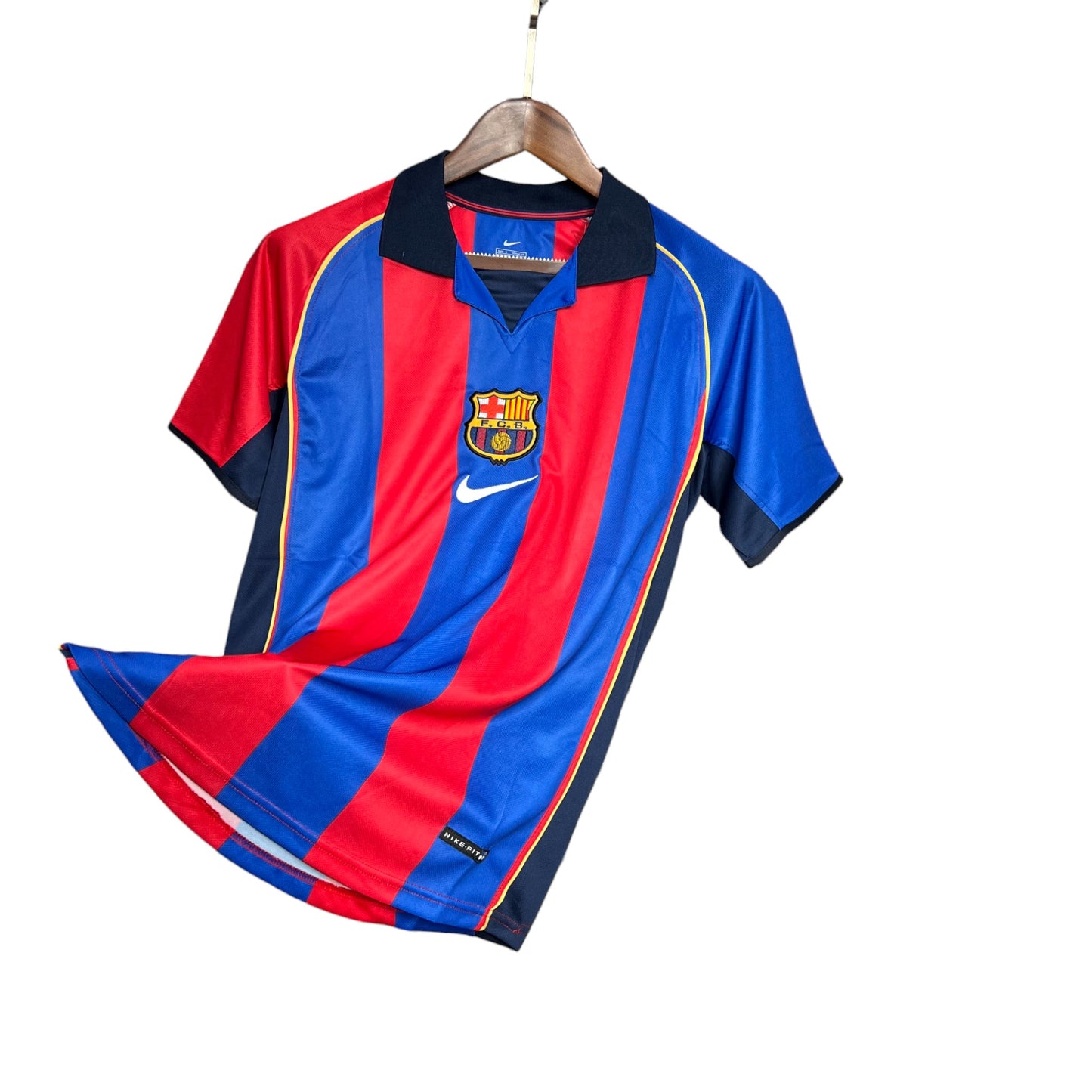 A FC Barcelona 2001/2002 Home Jersey hanging on a wooden hanger, displaying the red and blue striped pattern with the Barcelona crest and Nike logo.