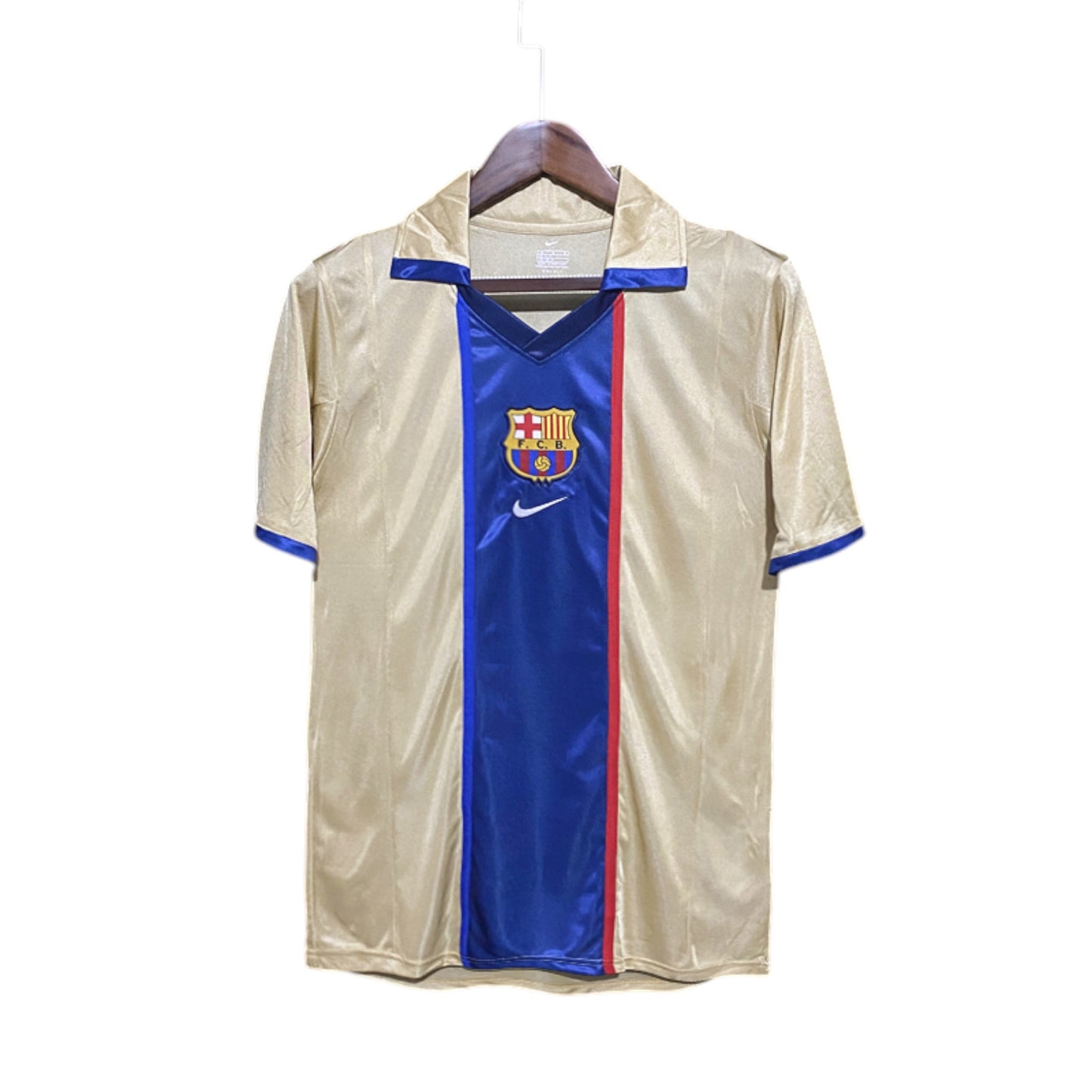 A FC Barcelona 2002/2003 Away Jersey hanging on a wooden hanger, predominantly gold in color with blue and red accents and the Nike logo.