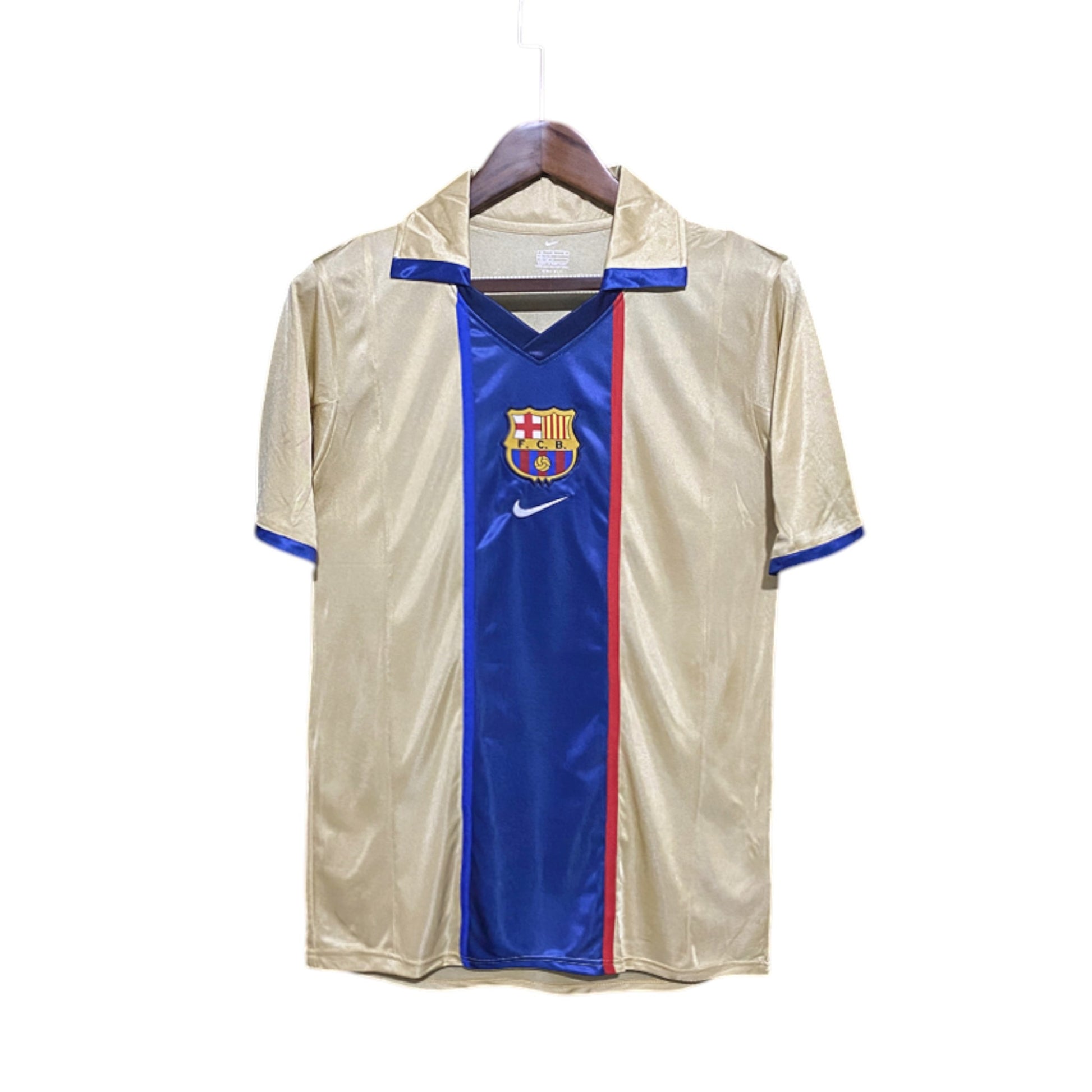 A FC Barcelona 2002/2003 Away Jersey hanging on a wooden hanger, predominantly gold in color with blue and red accents and the Nike logo.