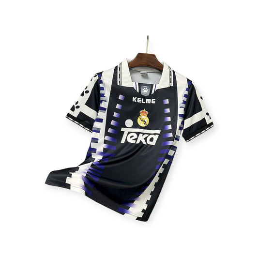 A classic soccer jersey with a geometric pattern, predominantly black with blue accents, and the brand name 'KELME' on the sleeves. The front features the 'Texa' logo.