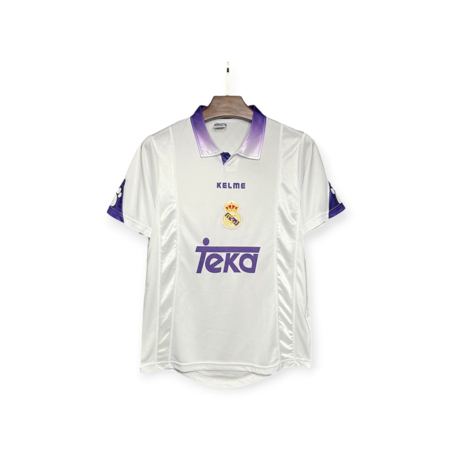Real Madrid 1997/1998 home jersey displayed on a mannequin, predominantly white with purple accents, featuring the team's logo and a sponsor's logo.