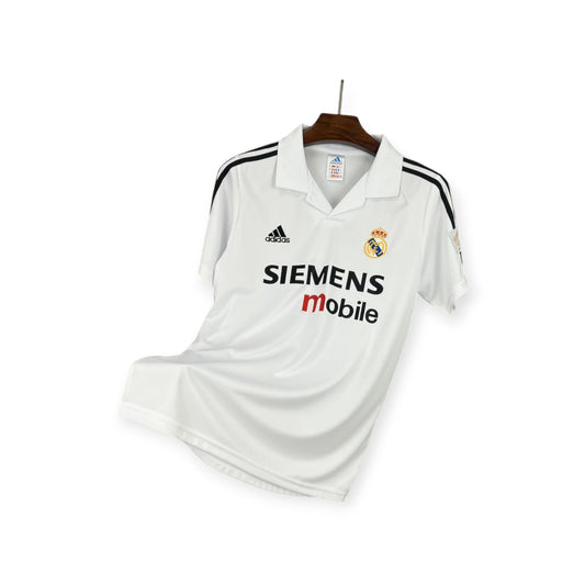 Real Madrid 2002/2003 Home Jersey displayed on a hanger, predominantly white with gold details, and sponsor logos including 'SIEMENS mobile'.