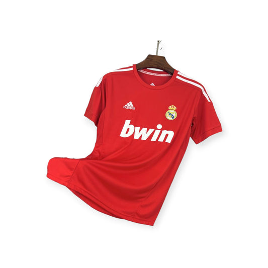 Real Madrid 2011/2012 away jersey displayed on a hanger, red with white accents and 'bwin' sponsorship logo.