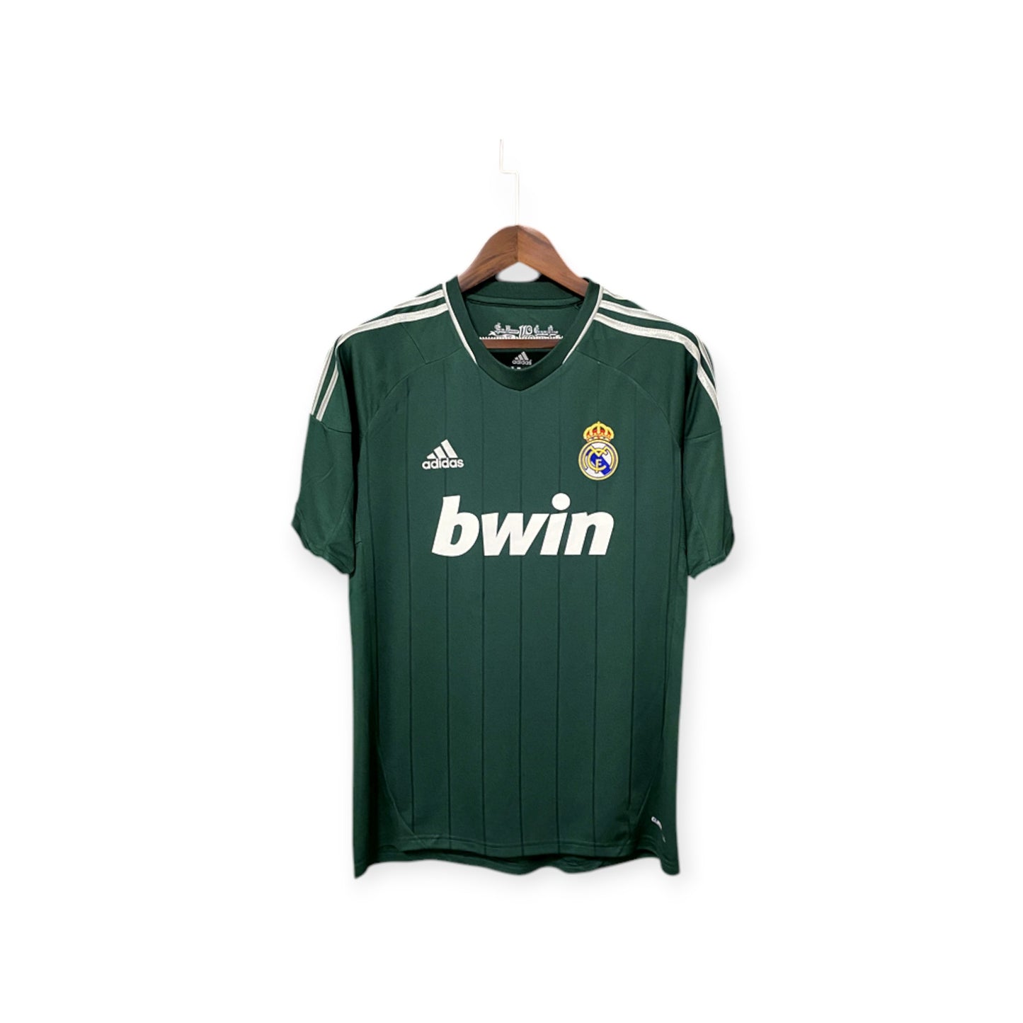 Real Madrid 2012/2013 Third Jersey hanging on a display stand, predominantly green with vertical white stripes, white collar, and the 'bwin' logo on the front.