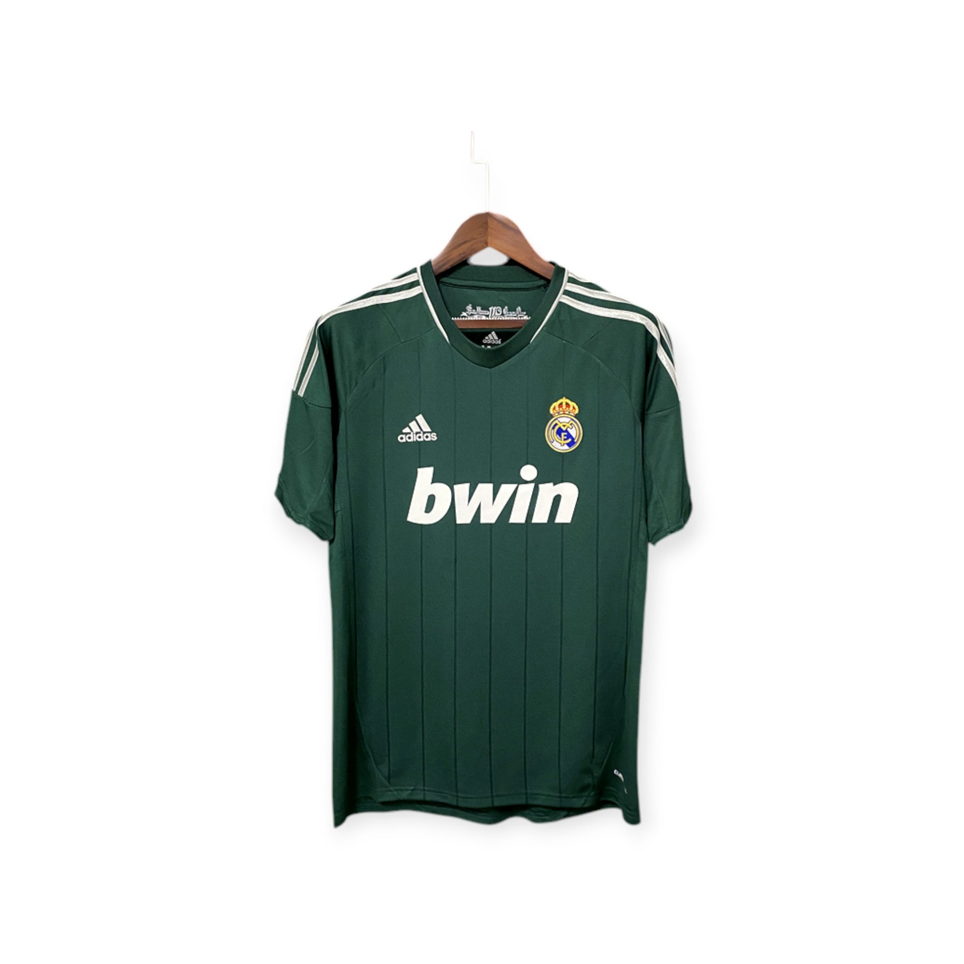 Real Madrid 2012/2013 Third Jersey hanging on a display stand, predominantly green with vertical white stripes, white collar, and the 'bwin' logo on the front.